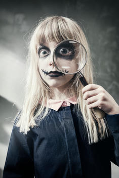 Young girl with scary make up looking trough magnifier glass