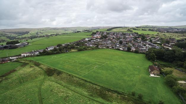 Aerial view of green field with football ground and suburbs on background with view of green lands.