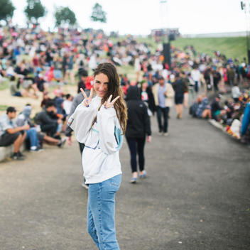 girl flashes peace signs while walking through a crowd during an outdoor concert