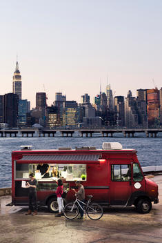 A group of people ordering Pizza from a Food Truck with Manhattan in the background