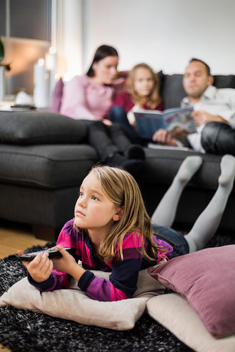 Girl watching TV on floor with family in background