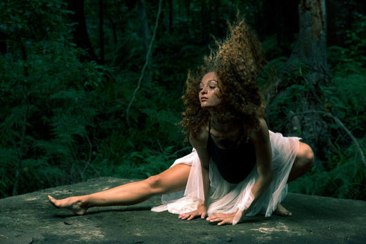 Dancer on all fours in the forest, throwing her curly hair back