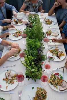 Overhead View Of People Eating On Outdoor Dinner Table With Herbs In Center