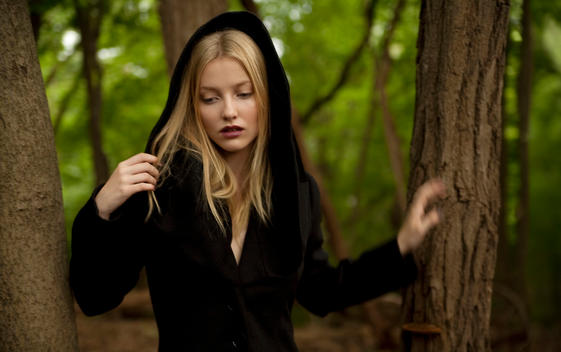 Blonde hooded woman standing in the woods.