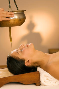 Young woman in spa with oil being poured on forehead, eyes closed