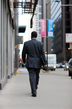 A Business Man Walks Down A Chicago Sidewalk Holding A Folder.