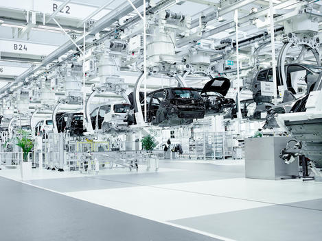 A production line of robot arms holding suspended automobiles in a modern white factory setting