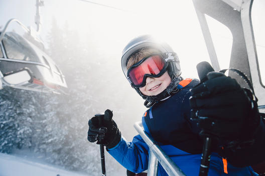 A young skier boy, wearing ski helmet and ski goggles, smiling to camera on a ski lift in the Tirol region in Austria.