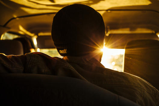 Person in car with sun shinning into lens wearing a beanie.