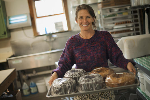 A woman in a kitchen carrying a tray of iced fresh baked cakes.