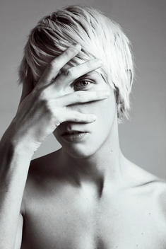 A young man with light hair hiding his face with his hand