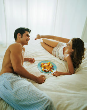 Couple eating fruit together on bed