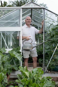 Portrait of senior man in his garden greenhouse with watering can