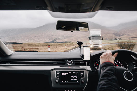 A drivers point of view from inside the car, with an oncoming large HGV lorry vehicle whilst driving away from a wet and windy Glencoe in the Scottish Highlands