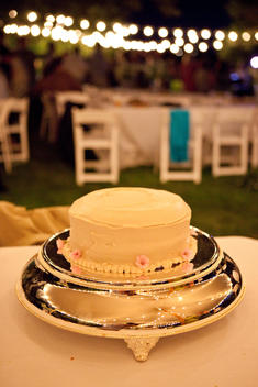 White Cake On A Silver Platter With White Lights Hanging In Background At Night
