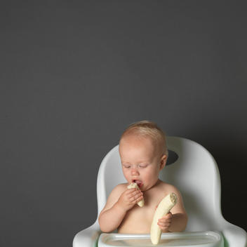 Baby In High Chair Eating A Banana