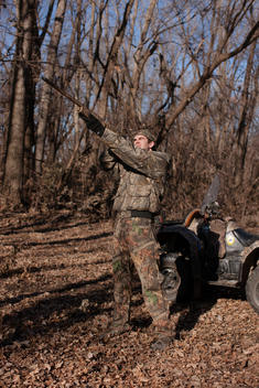 A hunter, dressed in camouflage, aims his gun on a hunt in the woods.