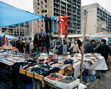 Market Stalls Selling Clothes In The Shadow Of Bombed Out Apartment Buildings Near The Central Square Of Grozny, Chechnya.