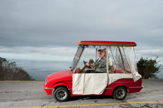 An old couple drive a red golf cart on a road overlooking the ocean on Catalina Island