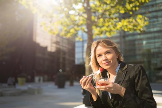 Portrait of young businesswoman outside city office eating strawberries