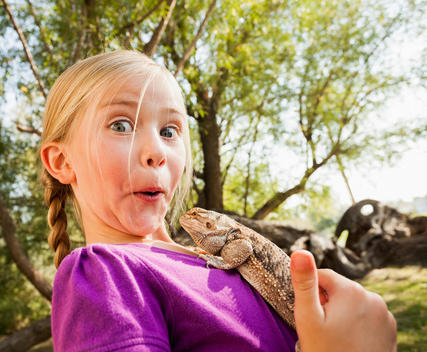 Little girl (4-5) surprised by lizard she is holding
