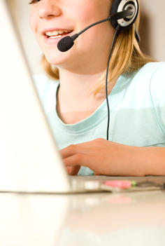Close up of smiling girl wearing earphones and microphone typing on a laptop