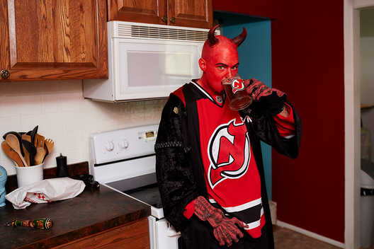 Ron Zastocki, who dresses as the New Jersey Devil, enjoys a cup of coffee in his kitchen while fully dressed in his New Jersey Devils outfit.