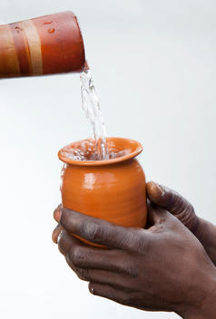 Two hands are grasping an orange cup as jug pours water into it