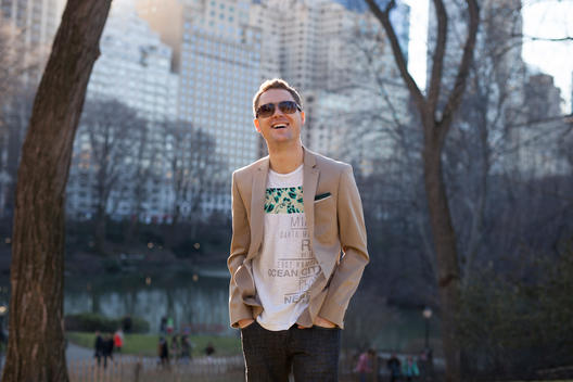 Portrait of business and tech entrepreneur Casey Kerr in sunglasses in Central Park on a sunny later afternoon with The Pond and buildings along 59th Street behind. NYC