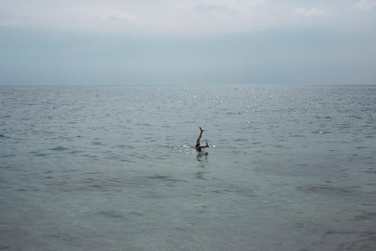 Person\'s feet sticking out of the ocean, surrounded by calm ocean water.