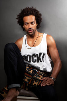 Studio photo of hipster athletic black male model sitting down in a tank top and urban clothing with dramatic light