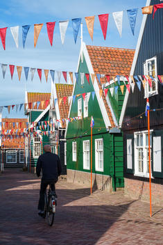 Man on bicycle rides past houses decorated for Koningsdag, or King\'s Day, with flags of Dutch national colors, Marken, North Holland, Netherlands