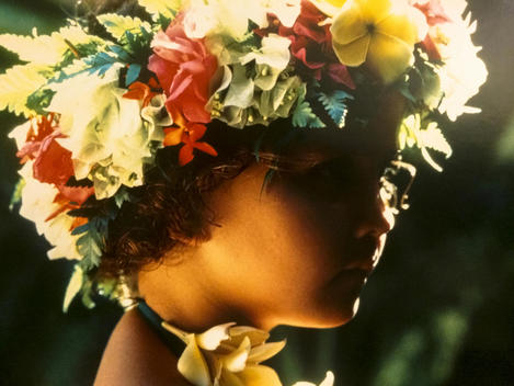 In French Polynesia a young girl wears a beautiful head band of flowers as the sun rims her profile and the colors of the flowers.