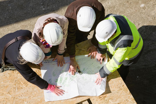 Architects meeting with building contractor at construction site to review blueprints
