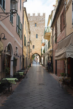 empty street with medieval tower and caf_ tables set out along the sides