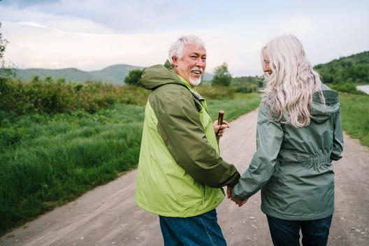 Portrait of a fit healthy older couple with grey silver hair laughing while walking together on a dirt road.