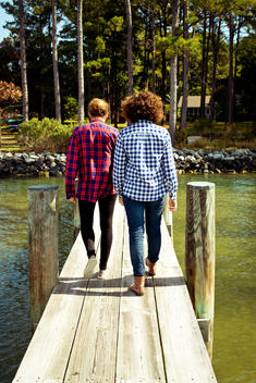 Two women in flannels walking down a dock