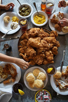 Aerial view of people sharing a meal of fried chicken, biscuits and corn at a table.