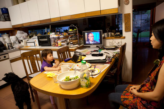 Child Having Dinner With Her Mother In The Kitchen, Dog And Tv In Background