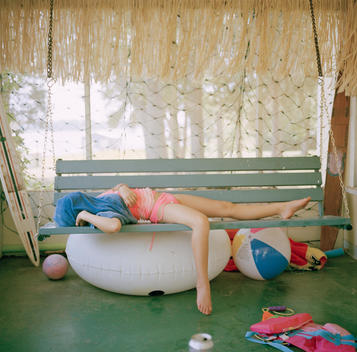 Lake Tyler, Texas: Portrait of a pouting, sulking, and annoyed young teenage girl covering herself with a towel as she lies on a swing in the back porch of her family\'s lake house after boating.