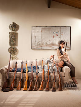 Man laying on couch with guns leaning against him while woman sits on the arm