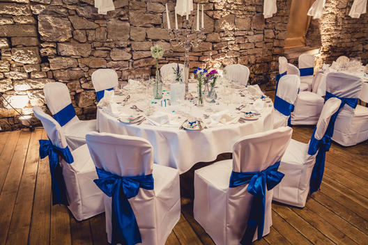 decorated wedding room, vintage stone wall, big chandelier, white covered chairs with a blue loop