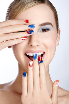 Caucasian model close up with her hands in front of her face. Her nails are painted in maritime colors, showing white, red, blue stripes, this was shot for nail it Magazine cover 2014