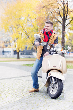 Poland, Warsaw, Mid-adult man sitting on motor scooter