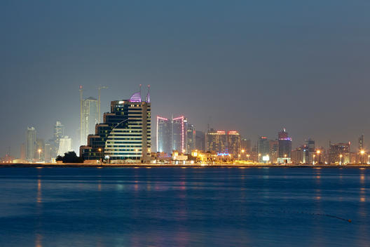 Cityscape of the modern architecture along the Corniche of Manama overlooking bay from Muharraq illuminated at night