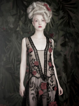 Portrait of a pale skinned woman in sheer black, floral dress and floral background.