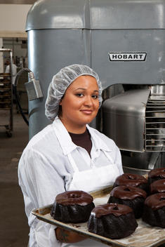 In a bakery a woman holds up a sheet of fresh chocolate cakes