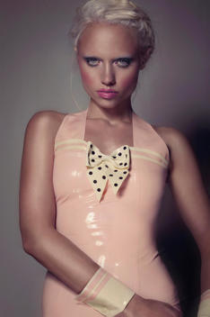 Blonde caucasian model hair up pink lips wearing a pink dress with polkadot bow, looking at the lens