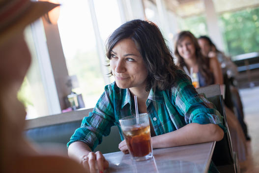 A woman seated at a diner looking out of the window. A long cool drink with a straw.