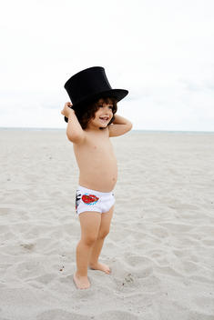 a baby toddler in his underwear panties on the beach wearing a top hat